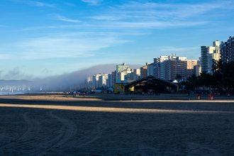 Orla da Praia Grande ao amanhecer, com edifícios altos à beira-mar.