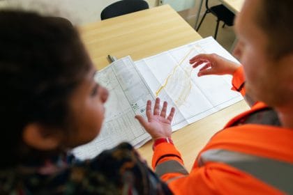 Duas pessoas analisam plantas de construção sobre uma mesa em um ambiente de trabalho.
