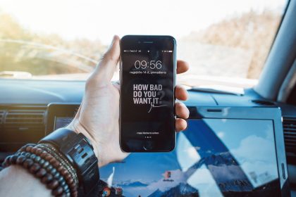 Mão segurando um celular dentro de um carro, representando a consulta digital de serviços de trânsito.