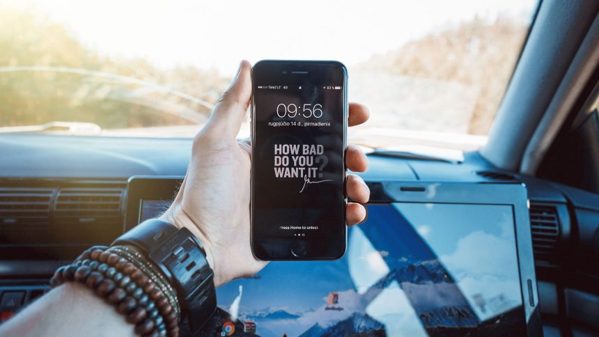 Mão segurando um celular dentro de um carro, representando a consulta digital de serviços de trânsito.