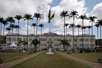 Fachada de um prédio municipal cercado por palmeiras sob céu nublado.