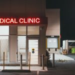 Entrada de uma clínica médica iluminada durante a noite, sem pessoas visíveis.
