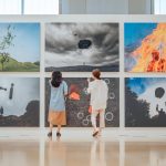 Duas pessoas observam obras de arte em uma galeria de exposição contemporânea.