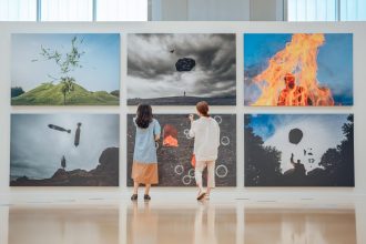 Duas pessoas observam obras de arte em uma galeria de exposição contemporânea.
