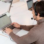 Atendente usando um laptop e fones de ouvido em um ambiente moderno de trabalho.