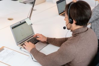 Atendente usando um laptop e fones de ouvido em um ambiente moderno de trabalho.
