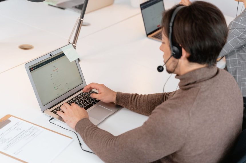 Atendente usando um laptop e fones de ouvido em um ambiente moderno de trabalho.