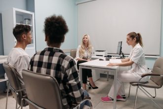 Profissionais de saúde conversam com pacientes durante uma consulta em um consultório médico.