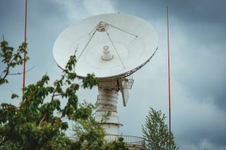 Antena parabólica de comunicação instalada em uma área cercada por vegetação, sob céu nublado.